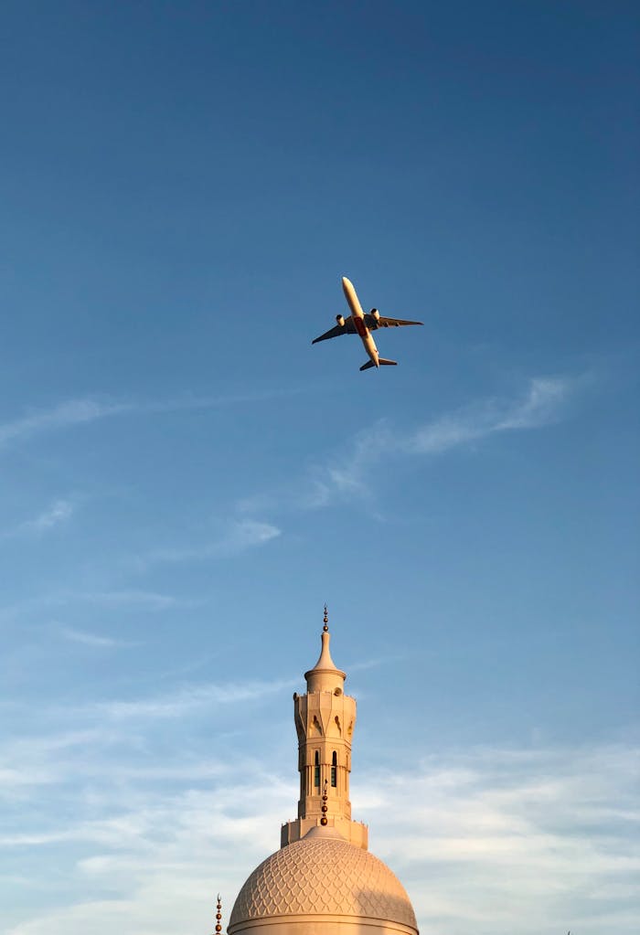 About A serene view of an airplane flying over a mosque dome with a clear blue sky background.